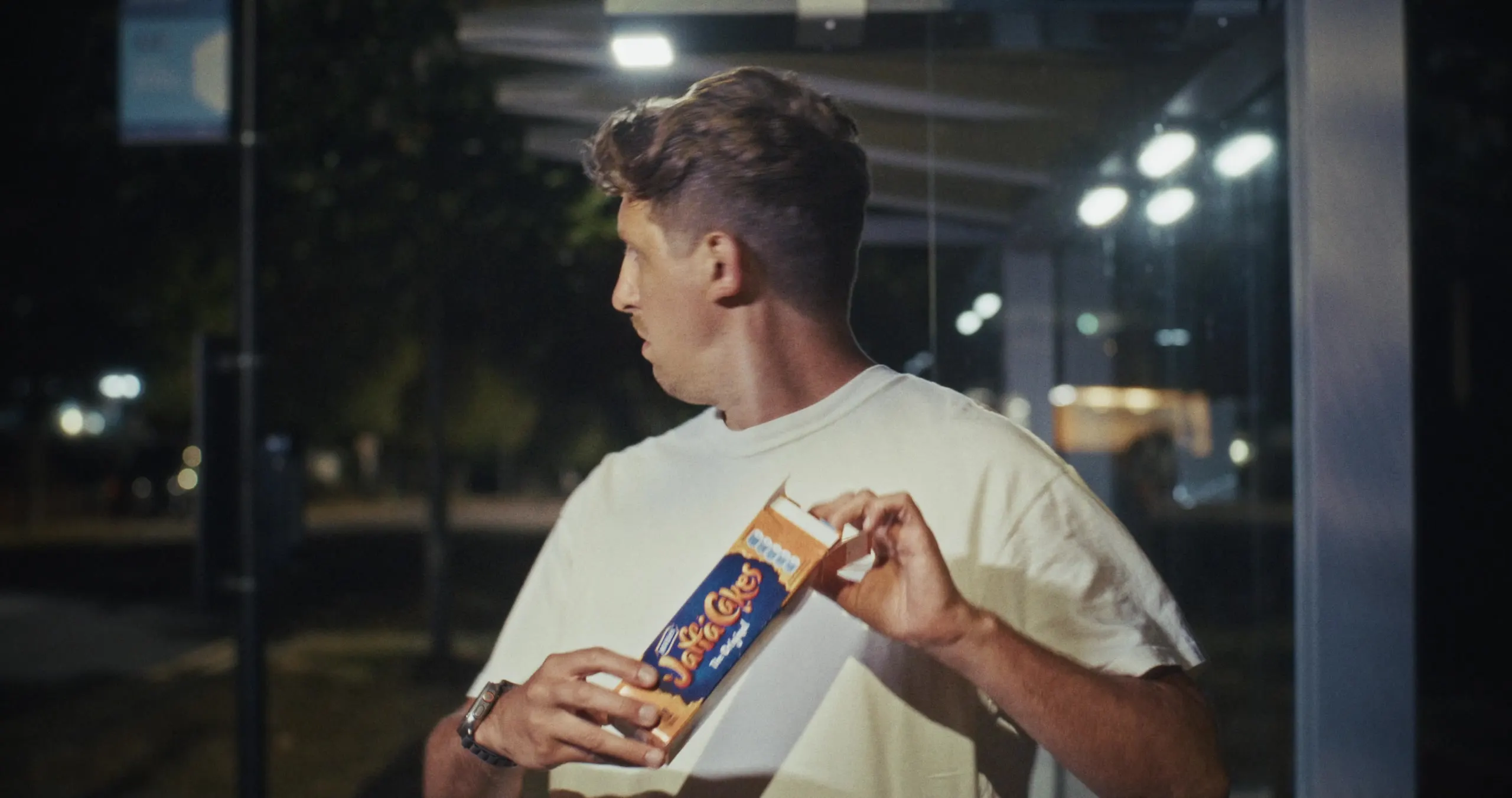 Mark G Smith in a bus shelter at night, holding a box of Jaffa Cakes and looking over his shoulder