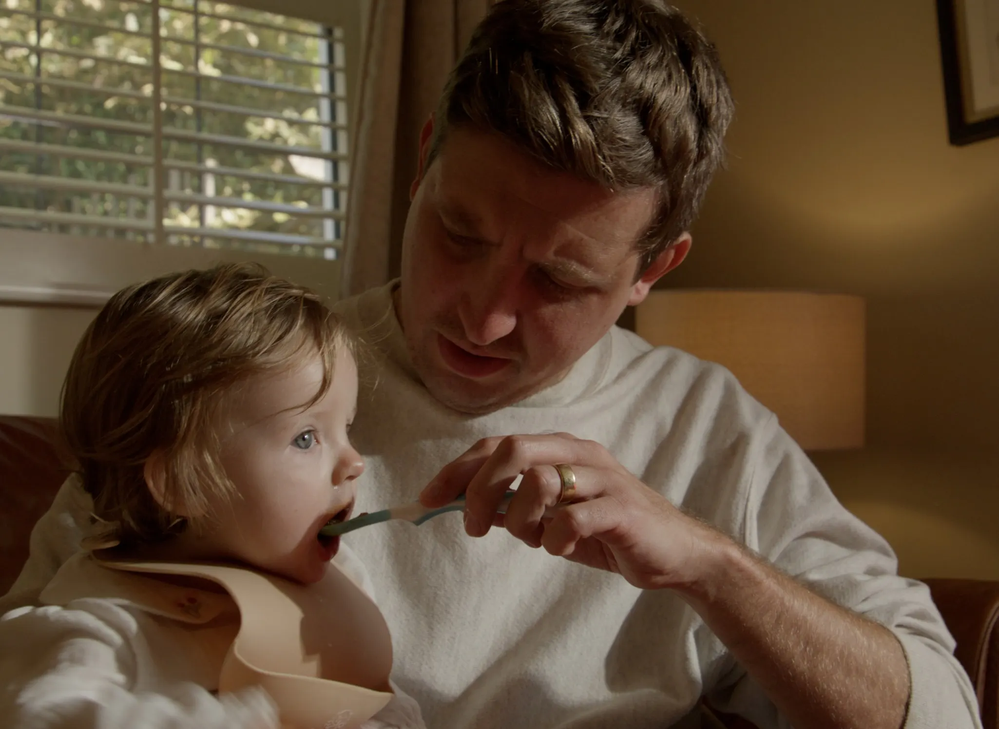 Mark G Smith spoon-feeds his daughter on the sofa
