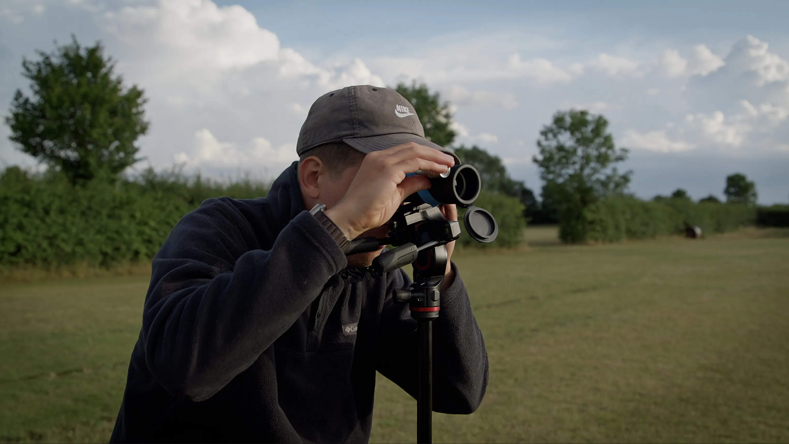 Mark G Smith as Peter looks through binoculars on a tripod in an open field