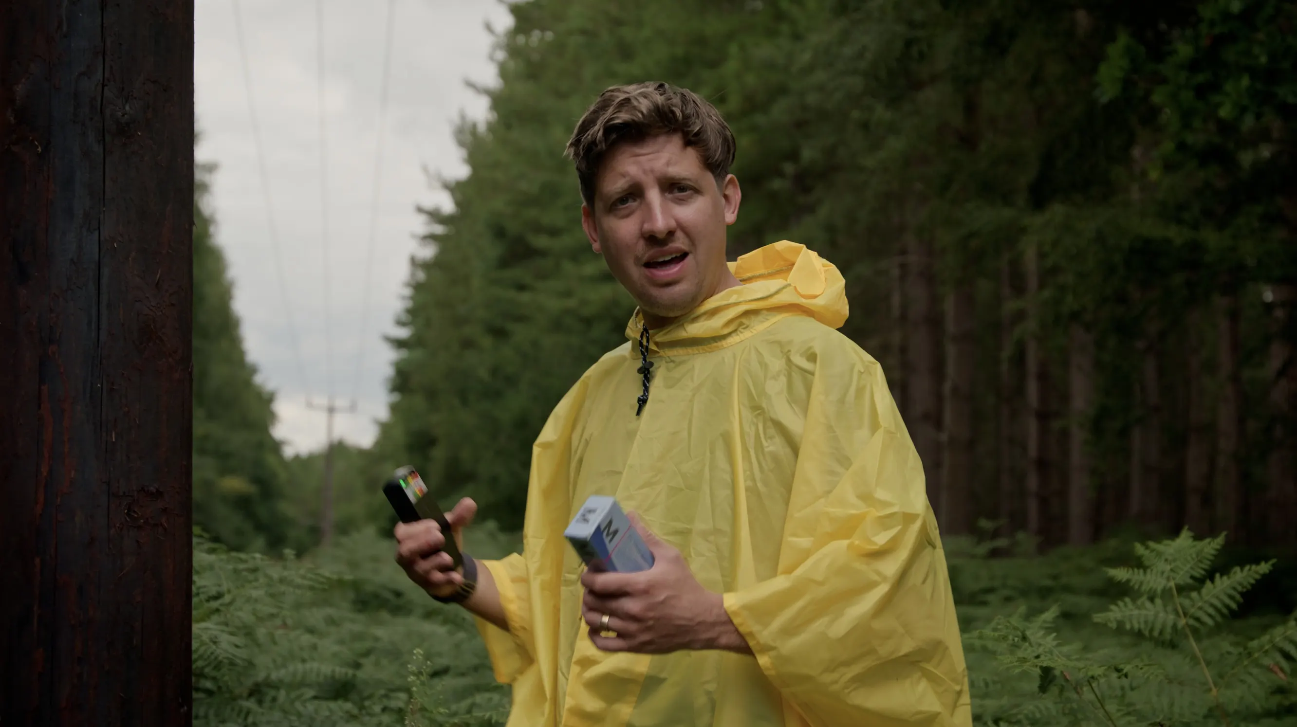 Mark G Smith as Peter holds up a meter and a box under the power lines
